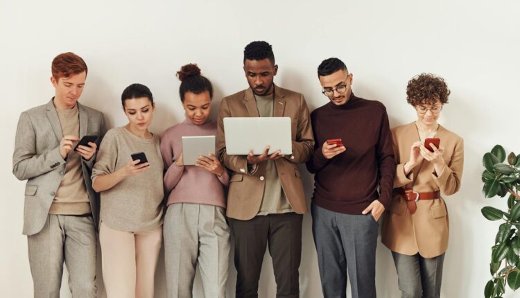 A diverse group of adults interacting with various devices in a stylish office setting, showcasing modern technology use.